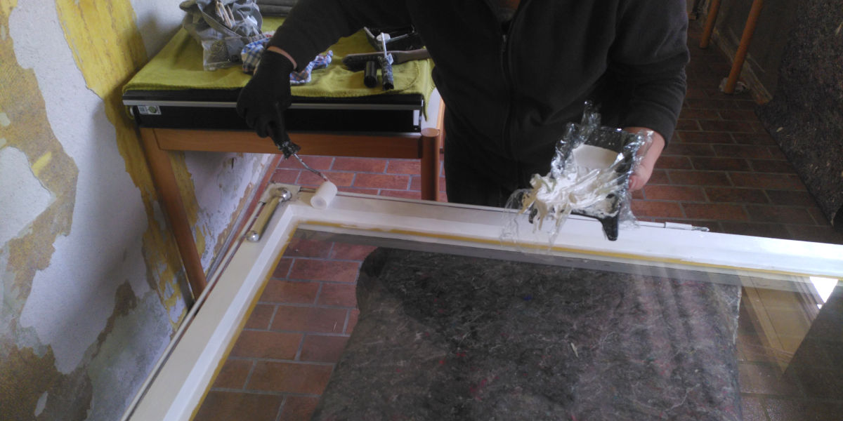 Jemand streicht in ausgebautes Fenster mit einer kleinen Rolle