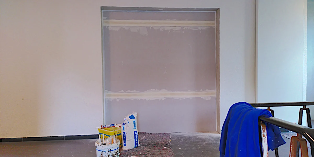 Person auf einem Gerüst verspachtelt die hohes Fenster